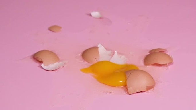 鸡蛋掉落并破裂在粉红色背景上。4k分辨率慢动作视频。