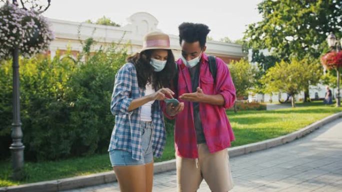 戴着防护面具的美国黑人男性正在询问女性正确的路线，在手机上显示地图