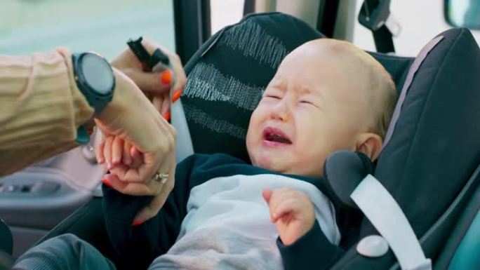 车内摄像头特写婴儿汽车安全座椅男婴出现在他母亲的手上，他把婴儿放在婴儿汽车安全座椅婴儿正在哭泣的母亲