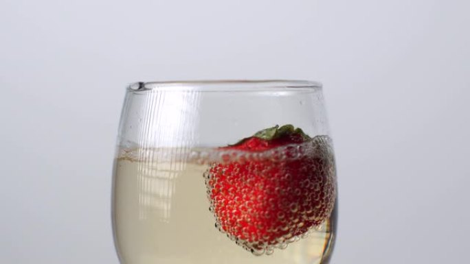 草莓在白色背景上掉入一杯香槟中的特写镜头