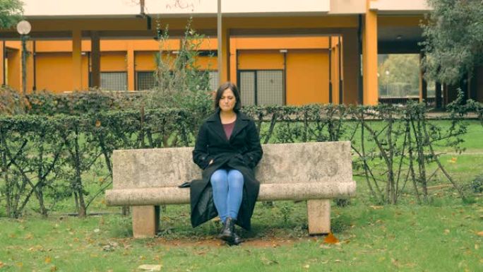 沮丧的伤心欲绝的年轻女子独自坐在公园的长凳上