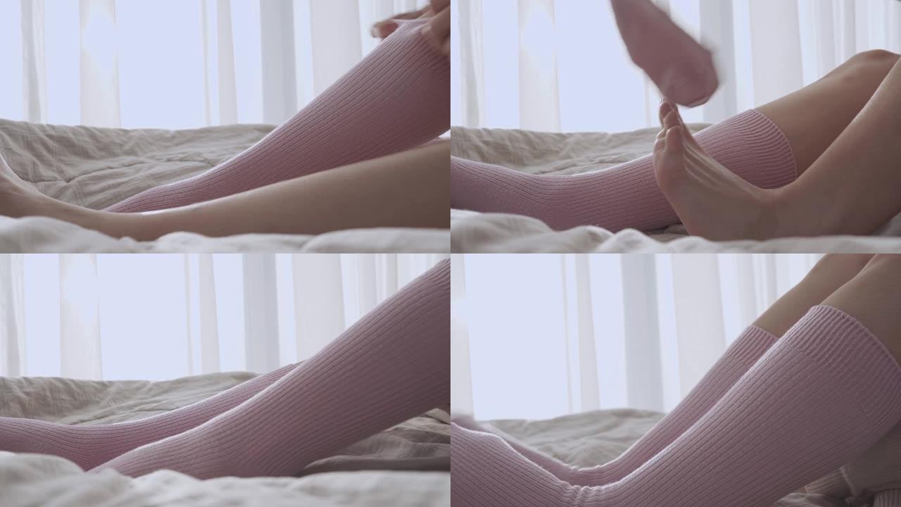 女人醒来时，穿着粉红色的袜子坐在床上，温暖的早晨阳光白窗帘，舒适舒适的卧室床单，保持体温，穿上袜子