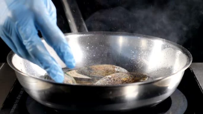 美丽的慢动作食物视频。厨师用蓝色手套将贝类放在热不粘煎锅上。到处都是油。高清
