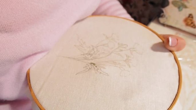 女人绣在手鼓上。在织物上绘制花卉图案。平均计划。针刺穿织物。