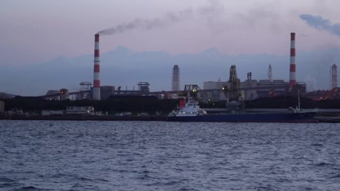 工业船在煤电厂前的码头卸煤，烟囱里冒出大量烟雾。