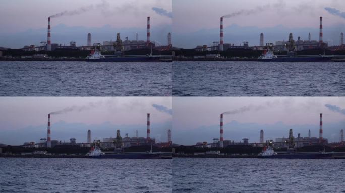 工业船在煤电厂前的码头卸煤，烟囱里冒出大量烟雾。