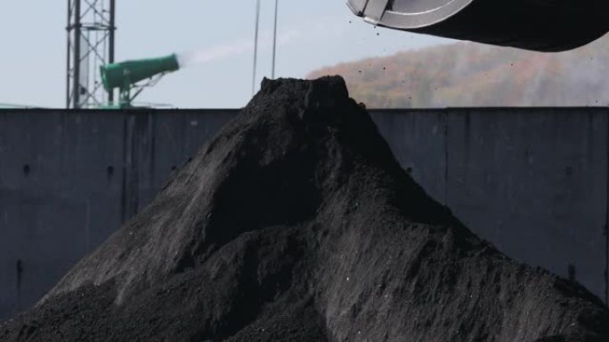 海运煤炭码头。一个大的桶将黑色的煤倒在一个大的煤堆上。