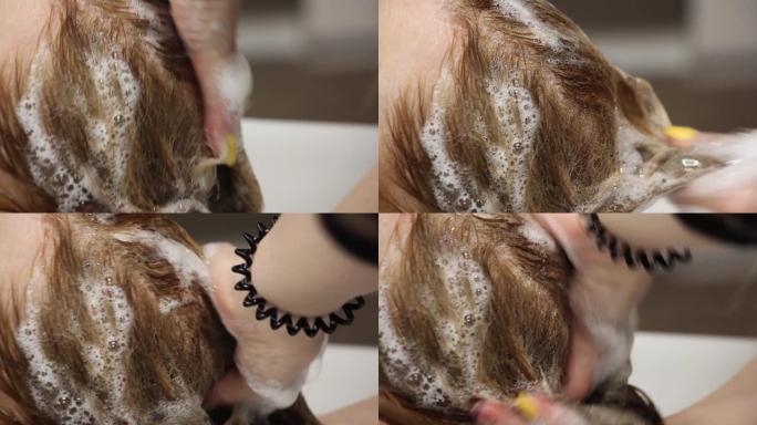 造型师用洗发水泡沫和按摩头为客户洗头，特写