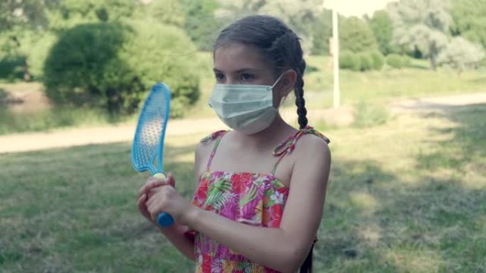 漂亮的小女孩戴着医用面具打羽毛球。病毒保护。