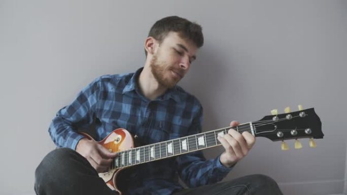 年轻的大胡子英俊的吉他手独自弹吉他。音乐家穿着蓝色衬衫在电吉他上演奏。音乐产业概念
