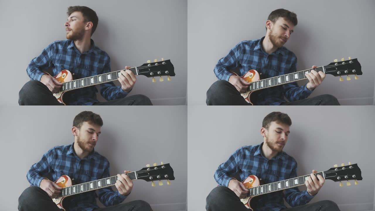年轻的大胡子英俊的吉他手独自弹吉他。音乐家穿着蓝色衬衫在电吉他上演奏。音乐产业概念