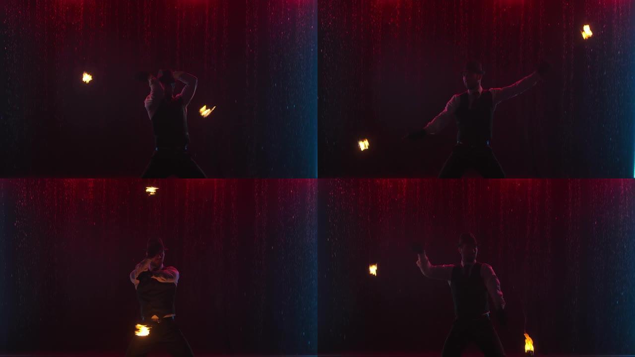 在雨中黑暗的工作室里，男性驯火师在一场激动人心的特写消防表演中。一个男人在慢动作中挥舞着火球的剪影
