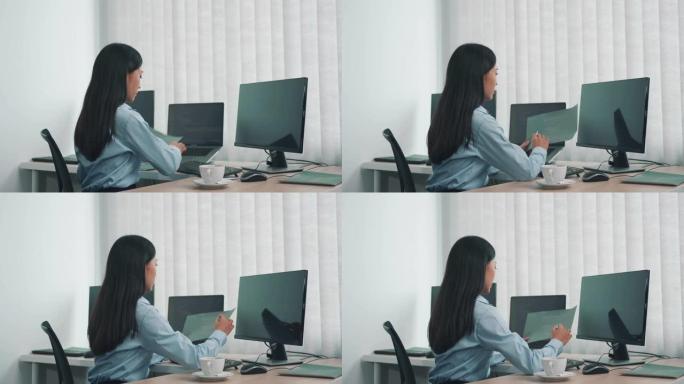 亚洲女性软件开发人员坐在电脑前看着屏幕上的电脑代码。