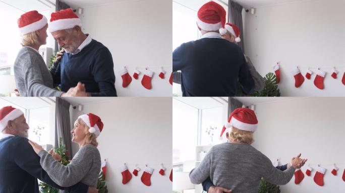 年长的高加索老人老头和女人戴着红色的圣诞帽，在客厅一起跳舞
