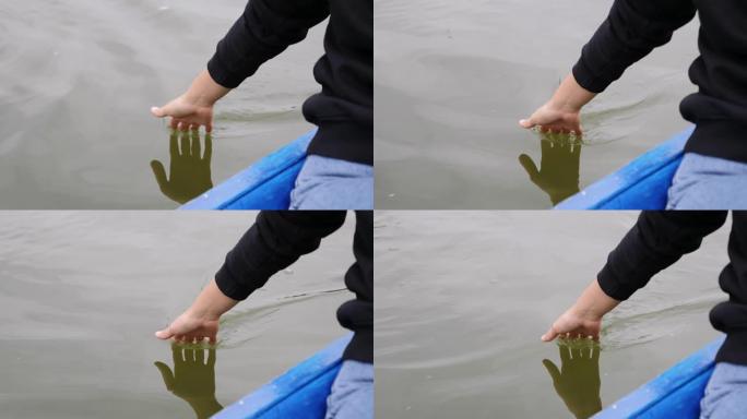 年轻女孩轻轻地抚摸湖上的水。女人在绿色的水上领着手掌。女人的特写手在公园里摸水。女人的手触摸湖上的水