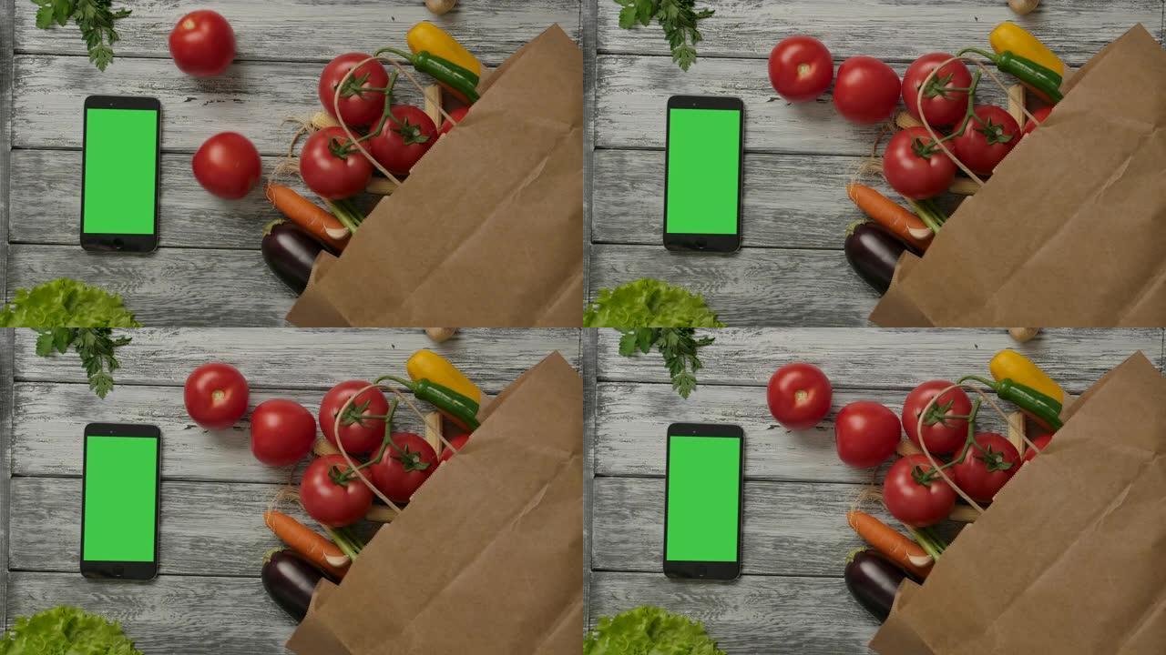 两个新鲜的西红柿在蔬菜和智能手机附近滚动