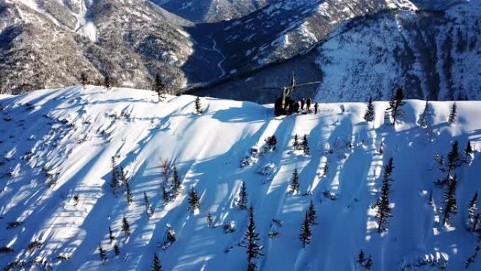 Actionsportlers被一架直升机降落在山顶。蓝蓝的天空中艳阳高照。背景中有一条山脉被雪覆盖