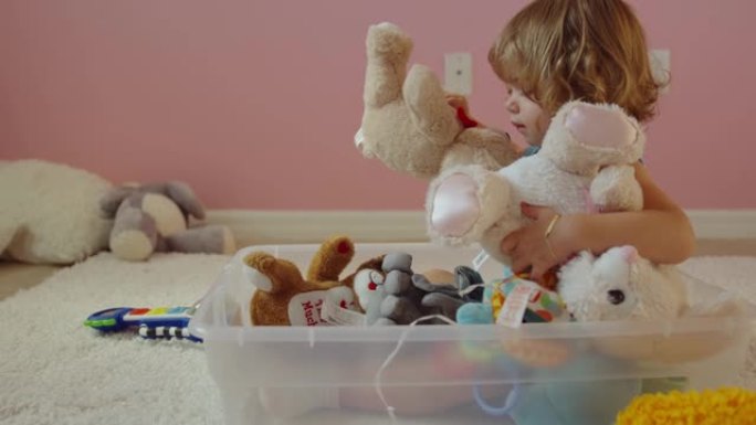 小女孩坐在塑料垃圾箱里玩填充动物玩具