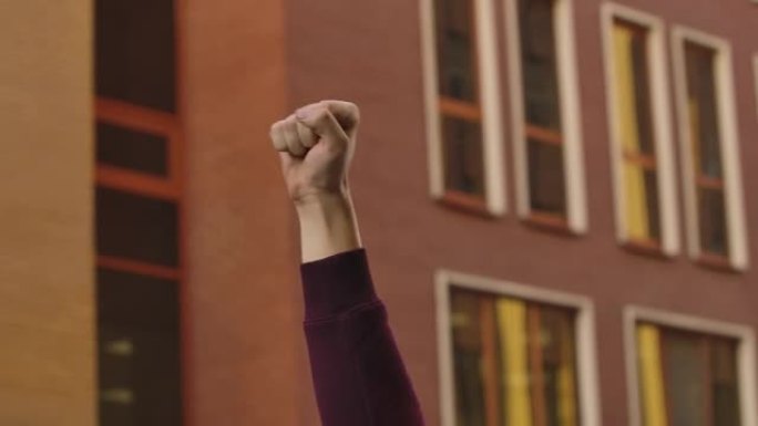 举起紧握拳头的男性的手，抗议的背景是一幢高层建筑。抗议种族主义和警察暴行。关闭了。慢动作