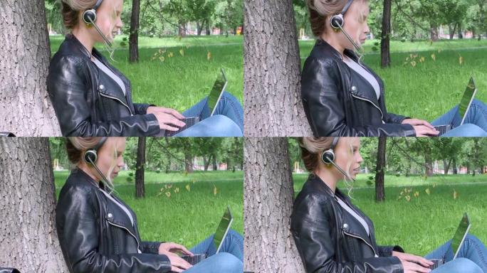 微笑的女人坐在城市公园里，戴着笔记本电脑和耳机进行在线对话。侧视图