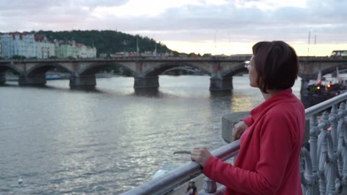 描绘旅行中的女性。年轻的成年美丽的女人享受宁静的日落在河边与柔和的自然黄昏光对着桥。欧洲之旅。美丽的