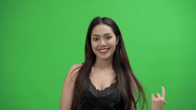 穿着黑色连衣裙的美丽亚洲女人在绿色屏幕上微笑。