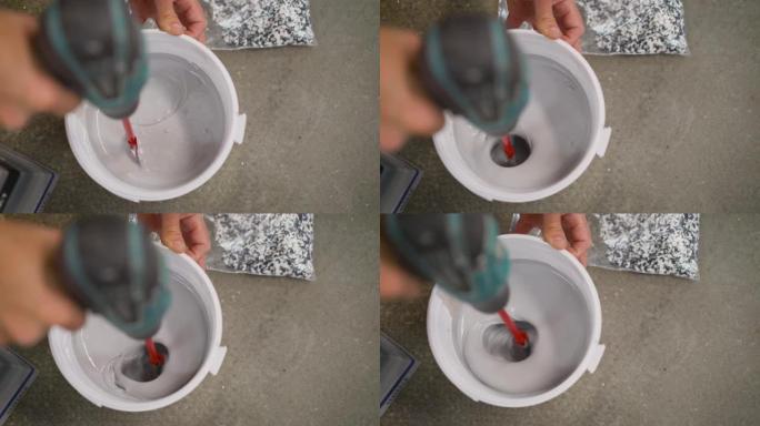用白色油漆、DIY工具和附件在铲斗上钻桨混合器。白色油漆与钻头混合在桶中。