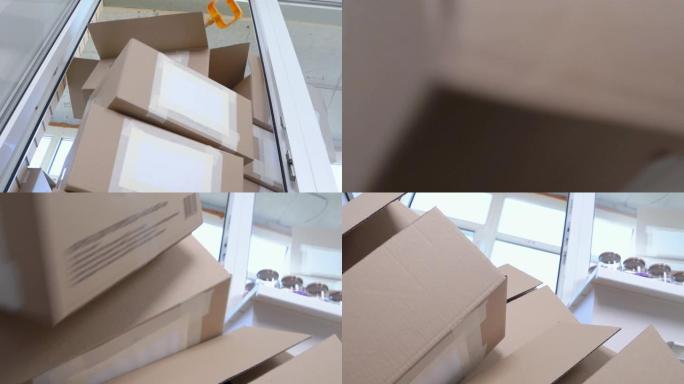 不稳定的带有文本标签的纸板箱山从阳台的门口掉下来，从下面看，崩溃了。搬家的东西，小公寓的存储问题