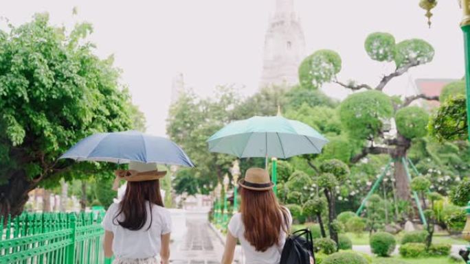 妇女和朋友在看地图。亚洲妇女享受曼谷Wat Pho在曼谷市的地标。两名亚洲妇女在雨天撑伞探索泰国主要
