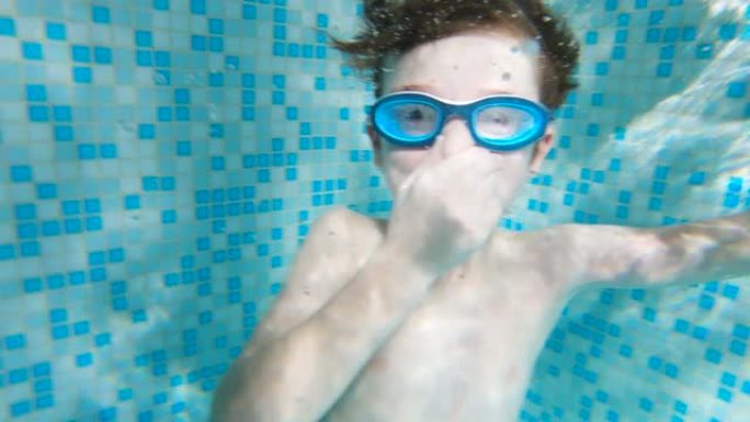戴着眼镜游泳的快乐男孩在山上的一家大型度假酒店的游泳池里捏着鼻子来学习潜水。水中有气泡。蓝色的水。家