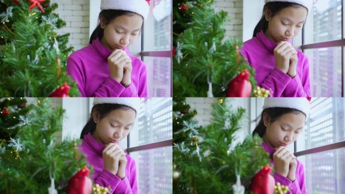 亚洲女孩在圣诞树旁祈祷上帝。
