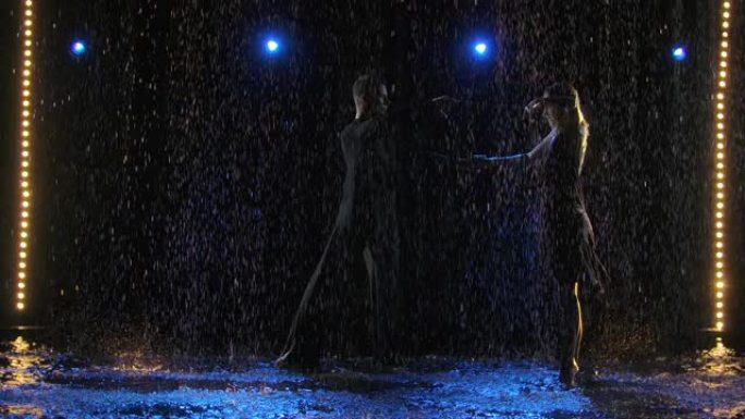 一对年轻的舞者在倾盆大雨中跳着热情的拉丁美洲bachata舞。黑色背景上一对穿着湿衣服的夫妇的剪影。