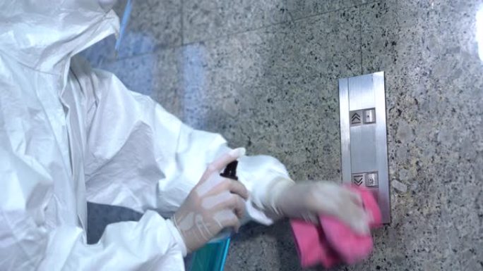 专家穿着ppe套装使用酒精消毒剂喷雾清洁办公室或工作场所的电梯按钮控制面板，以防止新型冠状病毒肺炎冠