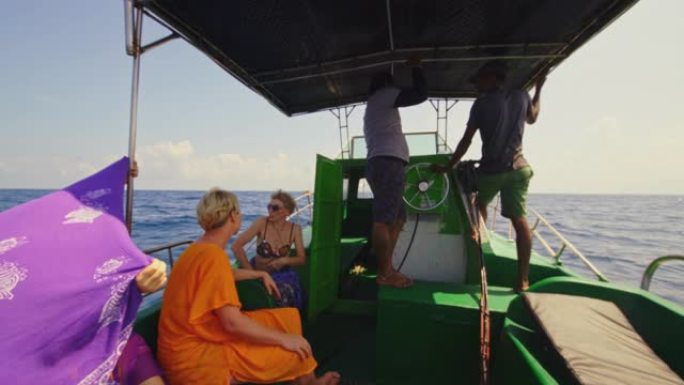 在斯里兰卡海岸的印度洋深海捕鱼之旅中，欧洲妇女的游客在帐篷下的阴凉处休息，并与当地向导和渔船上的船长