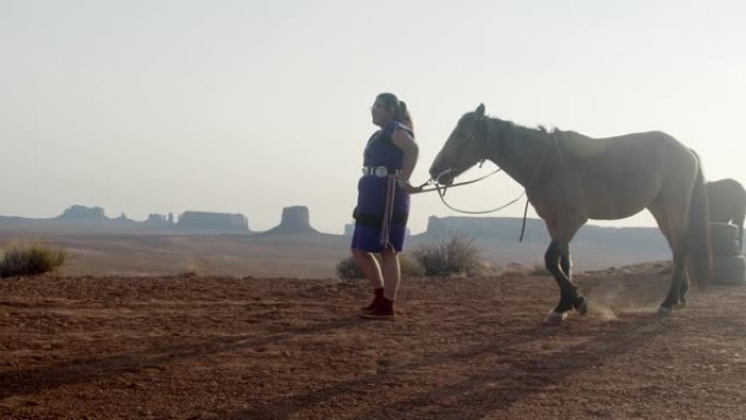 年轻的纳瓦霍人美国原住民女孩在黄昏时在亚利桑那州北部纪念碑谷的沙漠中骑着她的宠物马