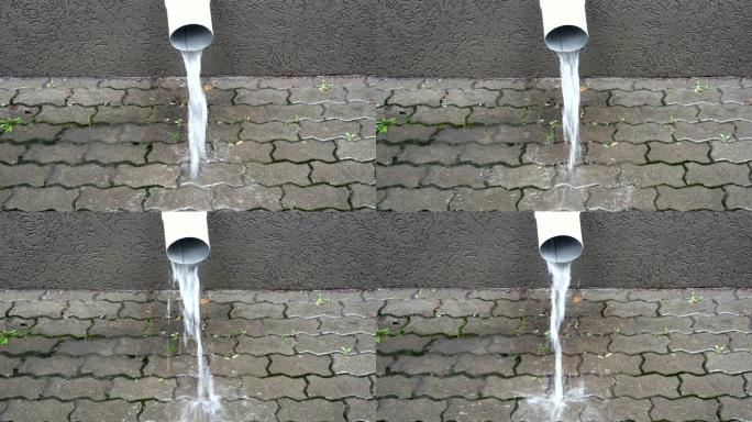 建筑物立面上的一条白色排水管的特写镜头，下雨时，人行道上有水流。城市里有雨。4K。