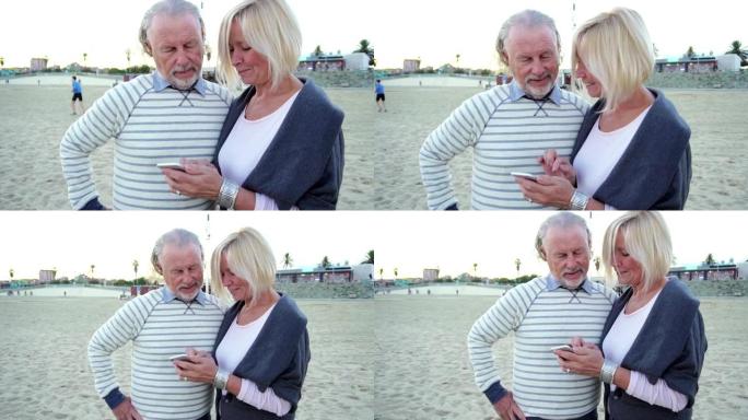 快乐的高级男女夫妇一起坐在海滩边的桌子旁，用手机聊天