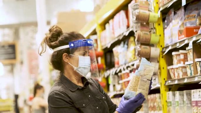 成熟的女人在超市过道上购买杂货，戴着防护口罩，手术手套和面罩