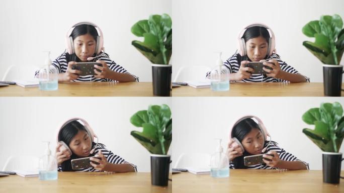 亚洲女孩戴着耳机，在家对着白墙玩智能手机在线游戏，生活方式概念。