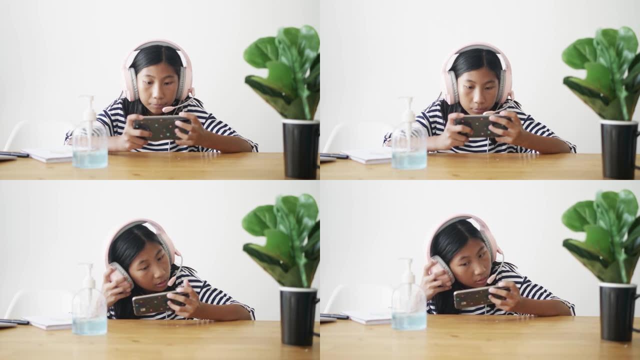 亚洲女孩戴着耳机，在家对着白墙玩智能手机在线游戏，生活方式概念。