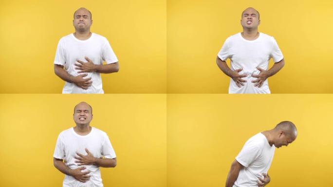 疲倦的不健康的秃头男人看着相机把手放在肚子上肚子疼穿着白色t恤孤立在黄色背景上。4k分辨率。
