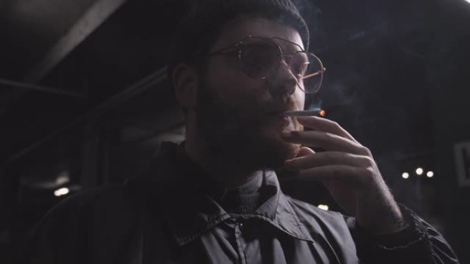 年轻的男性潮人在户外黑暗中抽烟，独自在街上抽烟