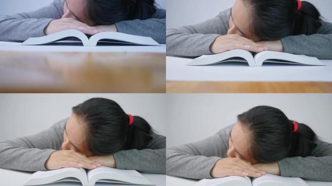 疲倦的学生女孩睡在家里的书本上。