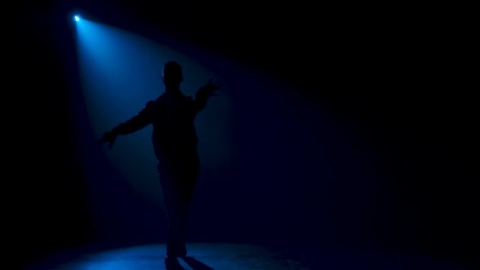 舞厅舞者男子在舞台上优雅地移动。蓝色霓虹灯中的深色轮廓。慢动作