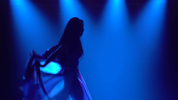 一个女孩在黑暗的工作室里跳舞的剪影，烟熏和蓝色霓虹灯。迷人的黑发女人，穿着英国国旗和水钻颜色的性感西