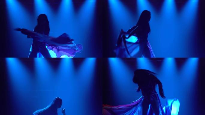 一个女孩在黑暗的工作室里跳舞的剪影，烟熏和蓝色霓虹灯。迷人的黑发女人，穿着英国国旗和水钻颜色的性感西