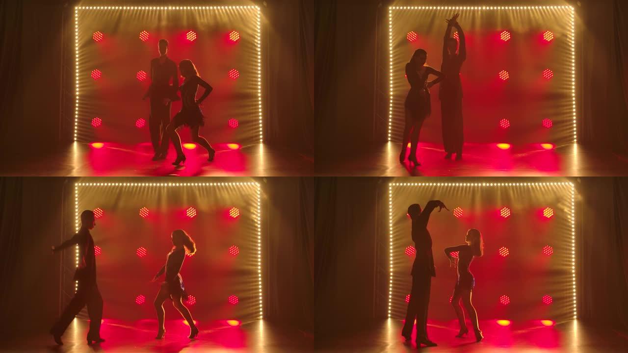 年轻美丽的夫妇跳舞性感的舞蹈恰恰恰舞。在带有红色聚光灯的黑暗工作室中，舞者的剪影。慢动作