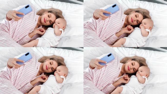 快乐的年轻母亲和小宝宝自拍使用智能手机。红色相机上的中等镜头