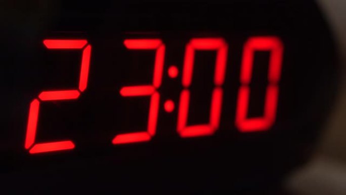 黑色数字时钟屏幕的特写显示23.00。黑色背景上闪烁红色数字。现代定时器系统和霓虹灯、电动报警装置