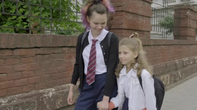 两个女孩姐妹牵手上学，穿着校服的孩子背着背包，背景城市街道